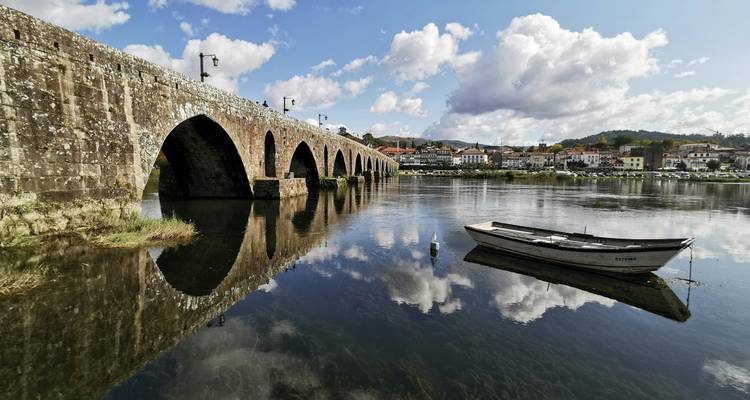 A scenic view of a stone bridge over a river with a boat and reflections.