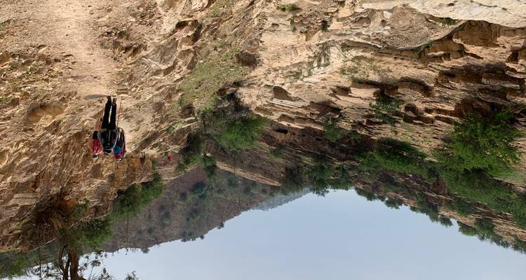 Hikers walking on a trail through rocky terrain with green shrubs.