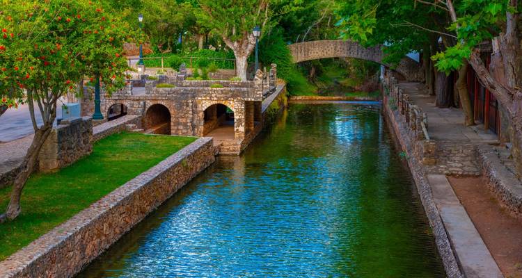 Charmant canal en pierre bordé d'arcades, d'arbres et d'un petit pont piétonnier aux eaux turquoise cristallines dans un village de l'Algarve.
