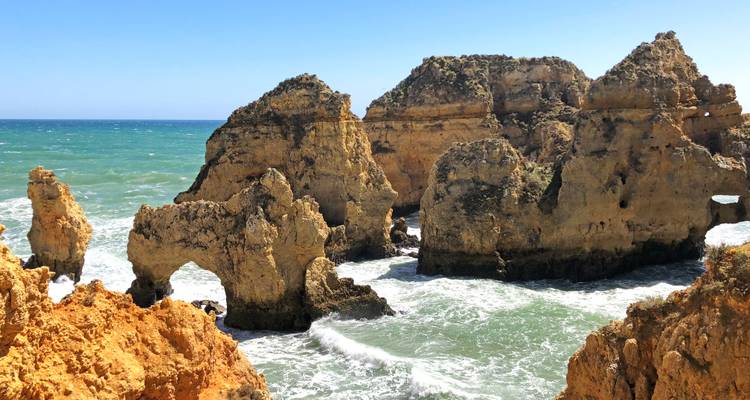 Spektakuläre Felsenbögen und Meereshöhlen, die in orangefarbene Klippen gehauen sind, überblicken türkisfarbene Atlantikgewässer.