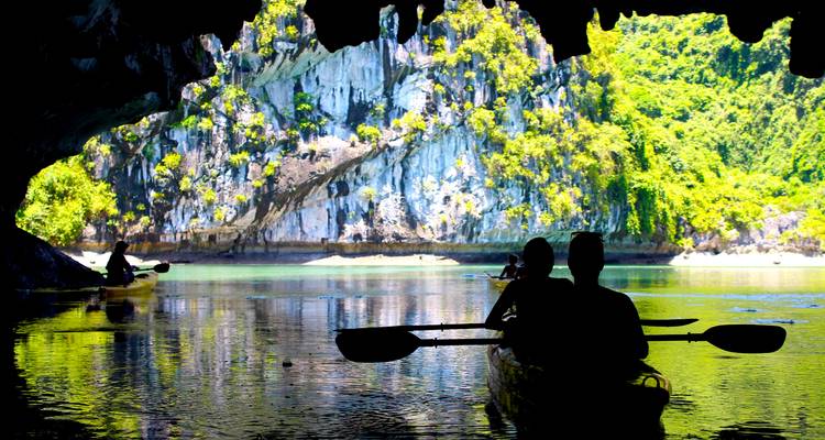 Kayakers exploring a cave opening to a scenic water view.