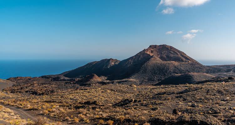 Paysage volcanique avec une montagne et l'océan au loin.