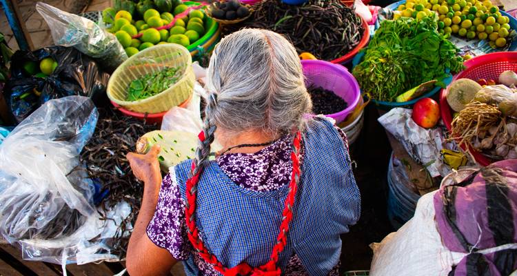 Scène de marché traditionnel avec une femme âgée préparant des légumes.
