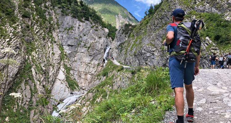 Trekker views a narrow gorge and waterfall while other hikers approach along the path.