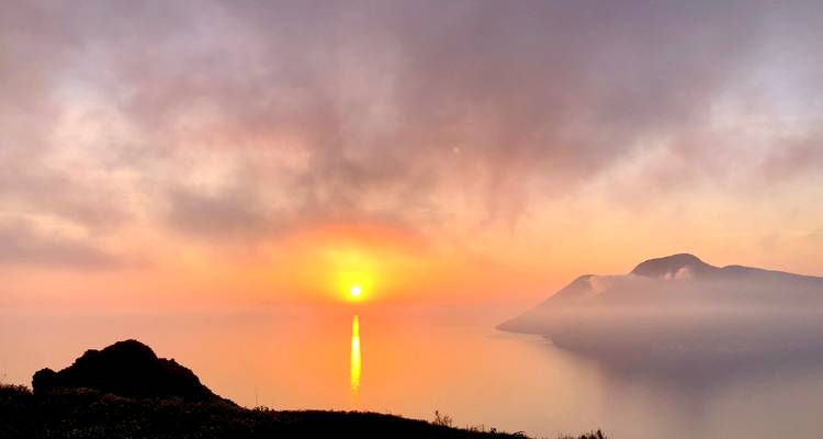 Sonnenuntergang über einer bergigen Küstenlinie mit leuchtenden Himmeln.