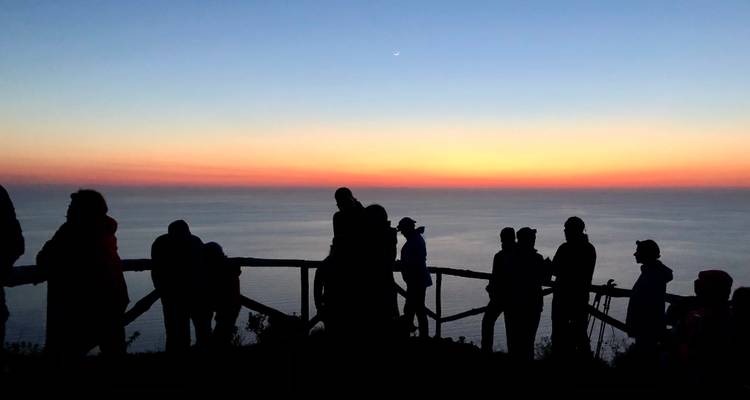 Silhouettierte Gruppe von Menschen, die einen Sonnenuntergang über dem Ozean beobachtet.