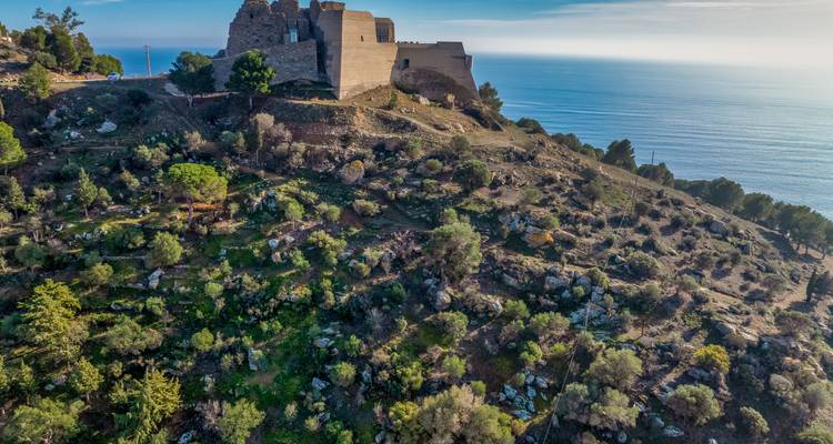 Una fortaleza de piedra en la cima de la colina domina una abrupta ladera costera verde que se encuentra con el azul del Mar Mediterráneo.