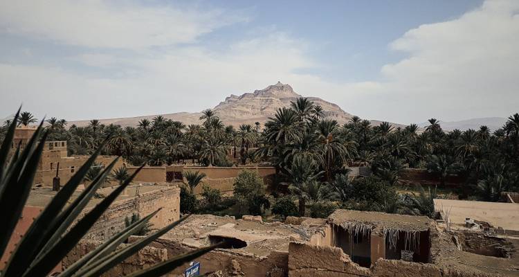 L'oasis palmée et la montagne désertique érodée s'élèvent au-delà des ruines en adobe.