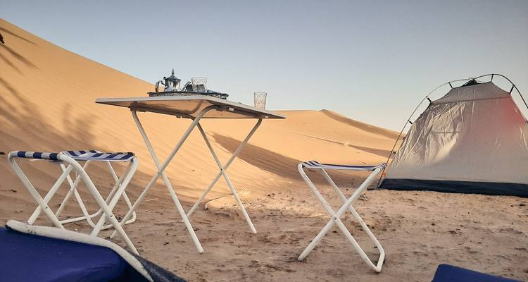 Configuration simple de camp désertique avec tente et table à thé face aux dunes de sable.