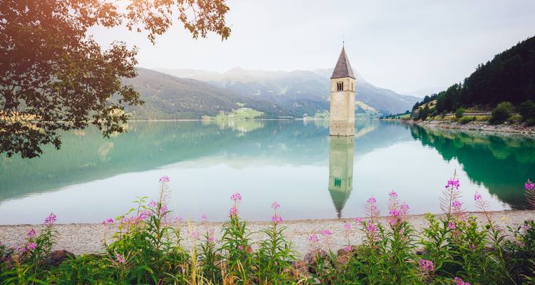 Ein Kirchturm, zur Hälfte in einem ruhigen See versunken, umgeben von Bergen.