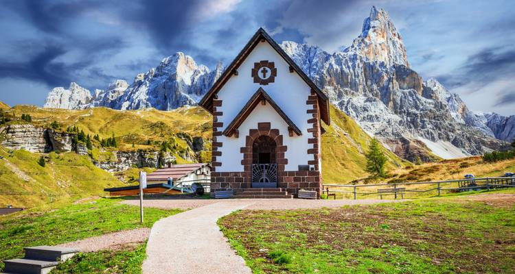 Capilla en un paisaje montañoso bajo un cielo dramático.