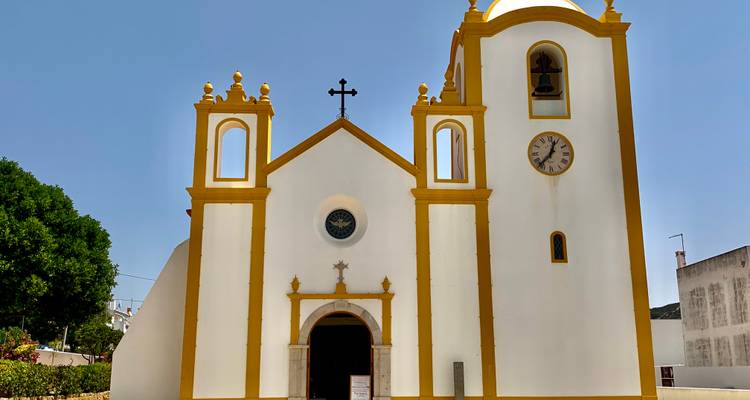 Église blanche avec garniture jaune, tours clocher jumelles et horloge sur un ciel bleu dégagé.