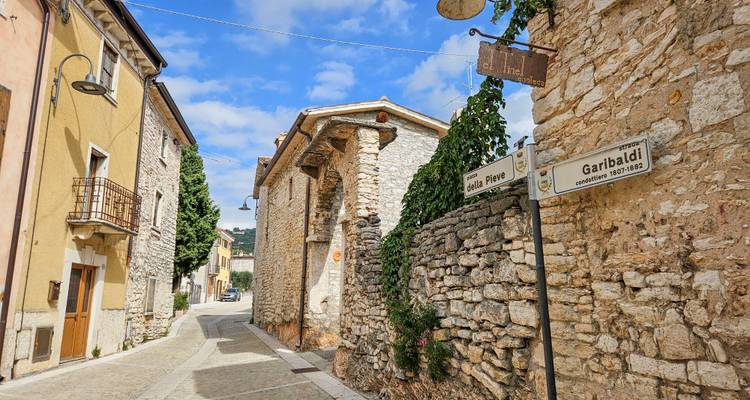 Une ruelle étroite et tranquille en pierre avec des bâtiments historiques et des panneaux de signalisation sous un ciel partiellement nuageux.