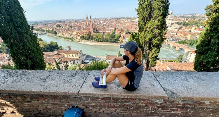 Femme assise sur un mur de pierre surplombant Vérone avec l'Adige, les toits et de grands cyprès.