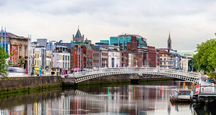 Rangée de bâtiments historiques colorés le long de la rivière Liffey avec le Ha'penny Bridge reflété dans l'eau.