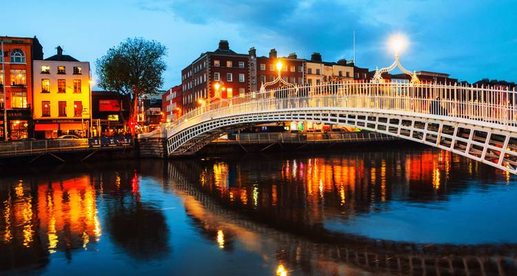 Vue nocturne du pont Ha'penny et des pubs riverains illuminés se reflétant dans les eaux calmes de la rivière.