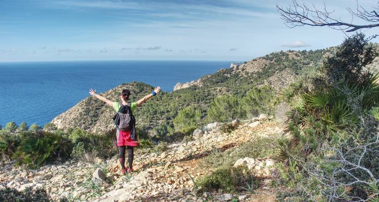 Hiker with arms outstretched enjoying a mountain and sea view.