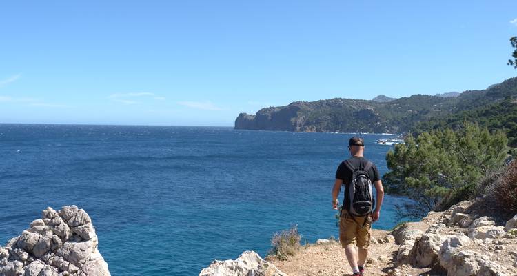Hiker walking along a rocky coastal path with a sea view.
