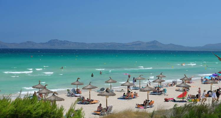 Une plage bondée avec des parasols et un arrière-plan montagneux.