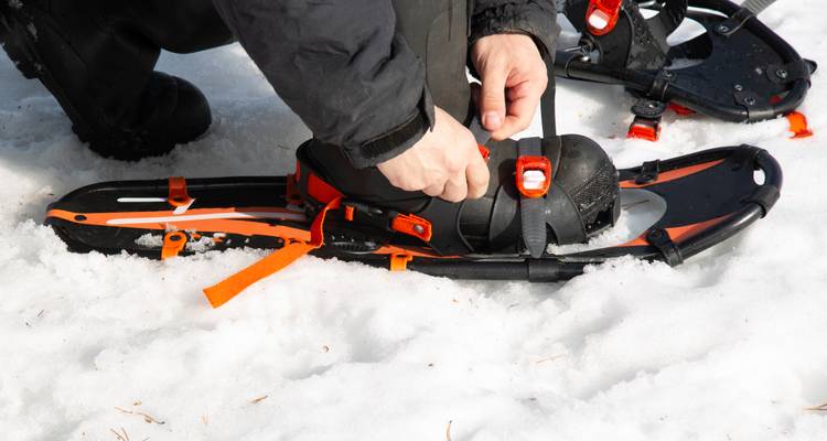 Personne attachant des raquettes sur un sol enneigé