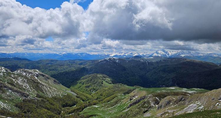 Scenic view of snow-capped mountains and lush green valleys under a partly cloudy sky.