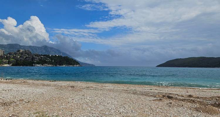Pebble beach with clear blue waters and mountains in the background.