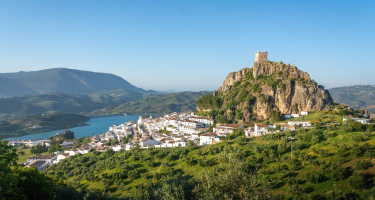 Dorp met een kasteel op een rotsachtige heuvel met uitzicht over grasachtige velden en een meer.