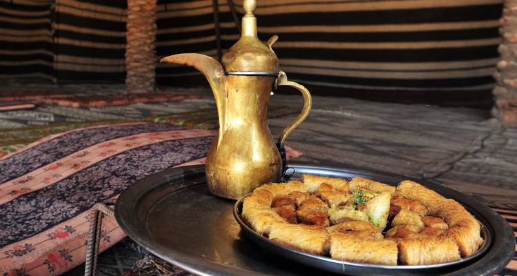 Kupferkaffeetopf und Teller mit Baklava-Gebäck auf einem traditionellen Tablett in einem Beduinenzelt.