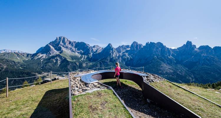 Person standing near a circular viewpoint with panoramic mountain views.