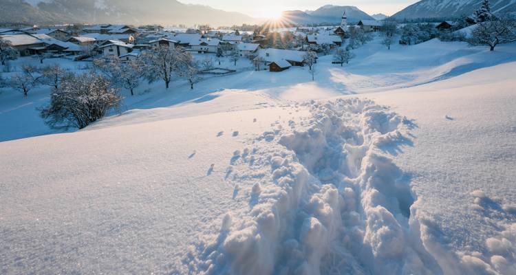 Piste d'empreintes menant à un village enneigé au lever du soleil