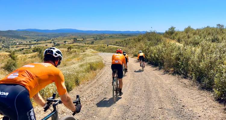 Cyclists on a dirt path in a rural landscape with hills in the background.