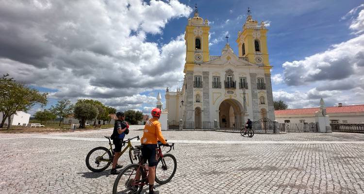 Cyclists near a historical church in a plaza.