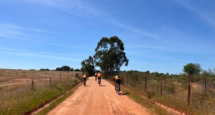 Group of cyclists riding along a red dirt road.