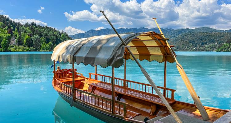 Traditionelles Pletna-Boot schwimmt auf dem türkisfarbenen Spiegel des Bleder Sees unter flauschigen Wolken.