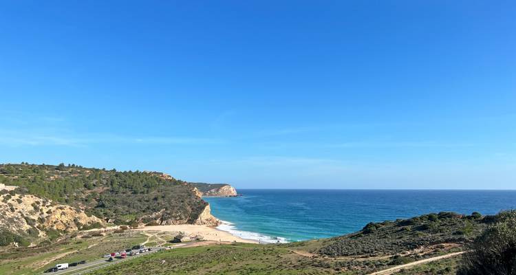 Large panorama côtier avec crique sablonneuse, promontoire et Atlantique bleu profond s'étendant jusqu'à l'horizon.
