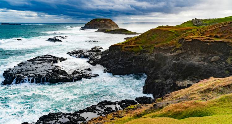 Eine felsige Küstenlandschaft mit tosenden Wellen und einem dramatischen Himmel.