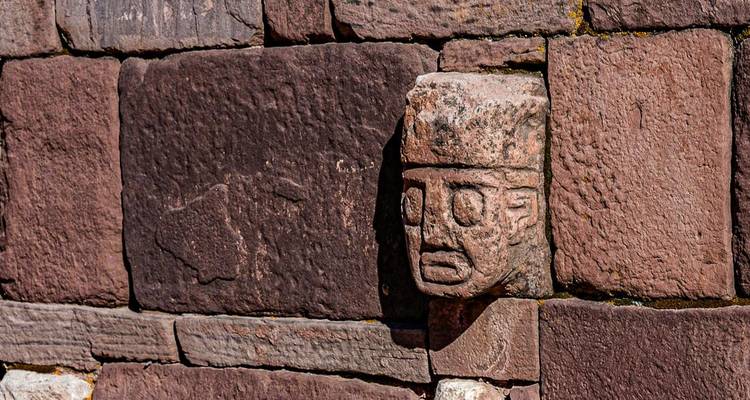 Stone wall with a carved human face, part of an archaeological site.