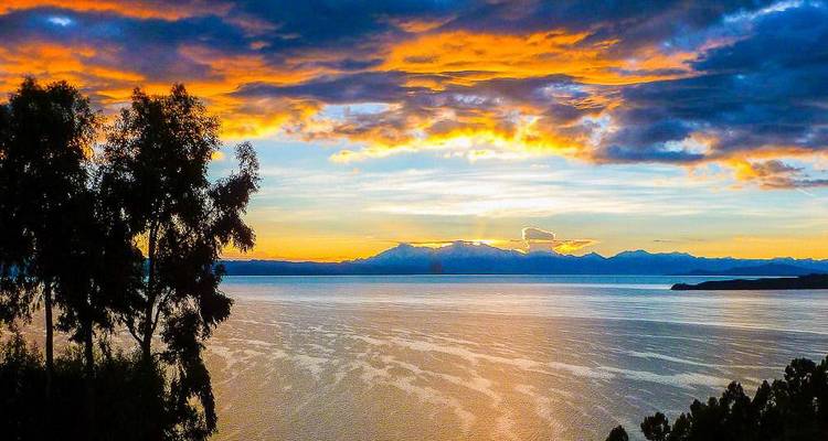 Sunset over a calm lake with silhouetted trees in the foreground.