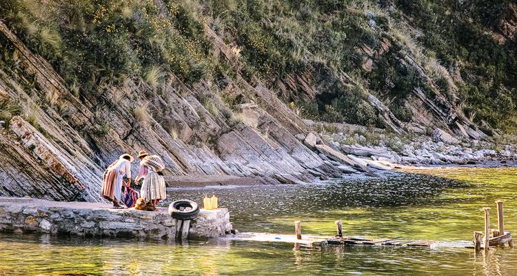 Local women in traditional dress by the lake with rocky cliffs.