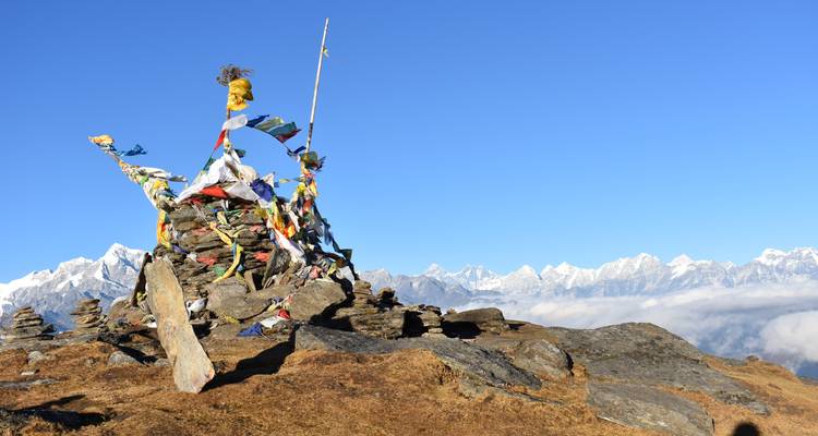 Sommet de montagne avec drapeaux de prière et vue panoramique sur les pics enneigés.