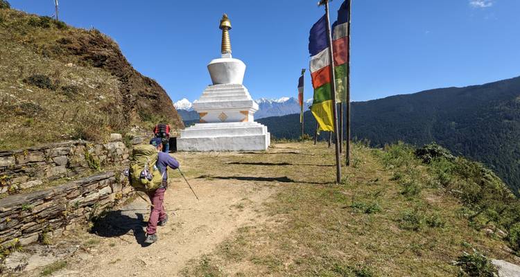 Randonneurs s'approchant d'un stupa blanc avec des drapeaux de prière colorés.