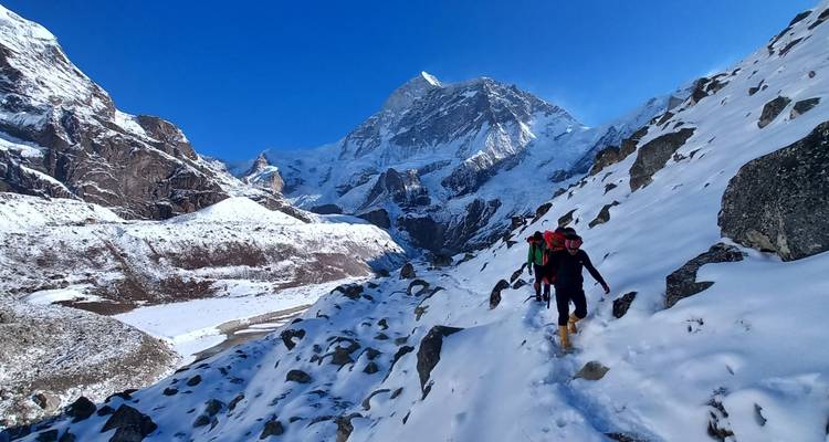 Wandelaars die lopen op een besneeuwde bergpaden met door de zon verlichte toppen op de achtergrond.