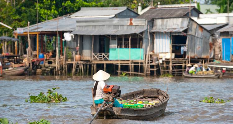 Person rowing a small boat near stilt houses.