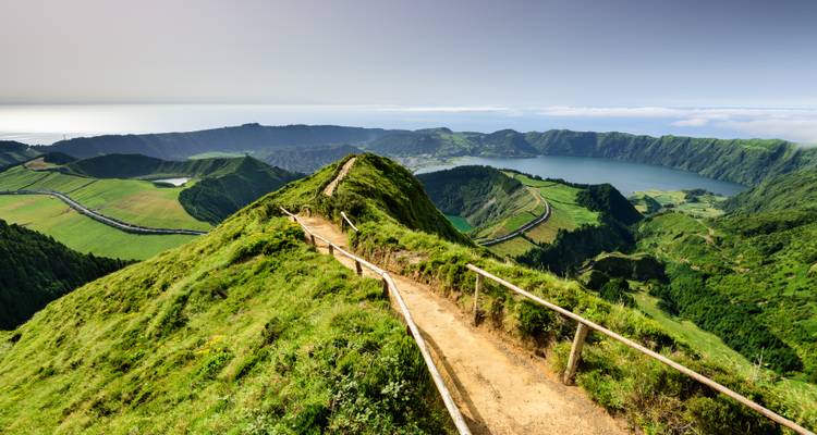 Sendero que lleva a una vista panorámica de un lago de cráter en un día soleado.