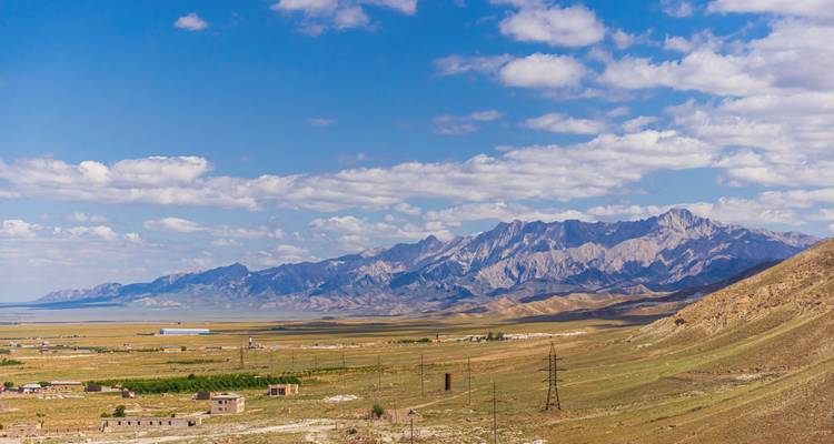 Scenic landscape with mountains and vast fields under a blue sky.