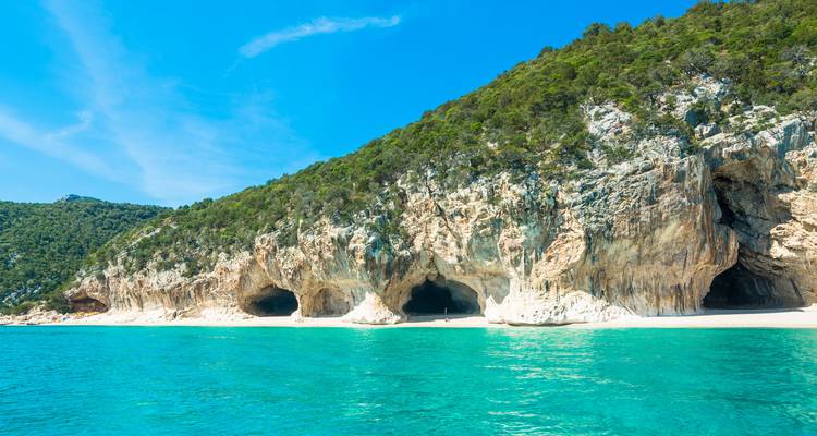 Des grottes marines creusées dans des falaises calcaires encadrées par des collines boisées et des eaux turquoise éclatantes.
