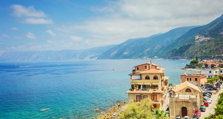 Una escena costera pintoresca con un mar azul y montañas distantes bajo un cielo suave.