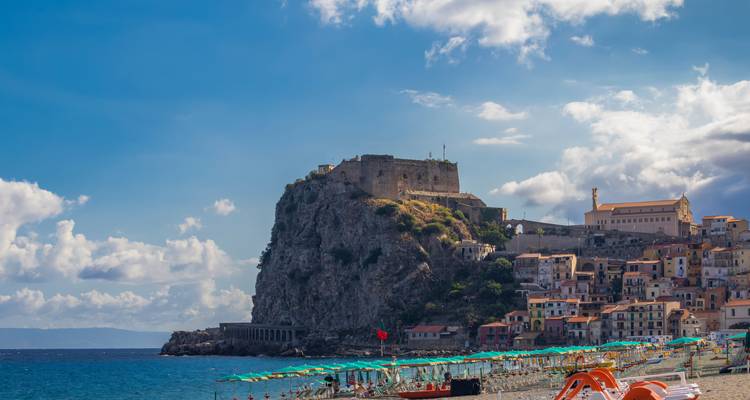 Un pueblo enclavado bajo una colina rocosa con casas coloridas bordeando la costa.