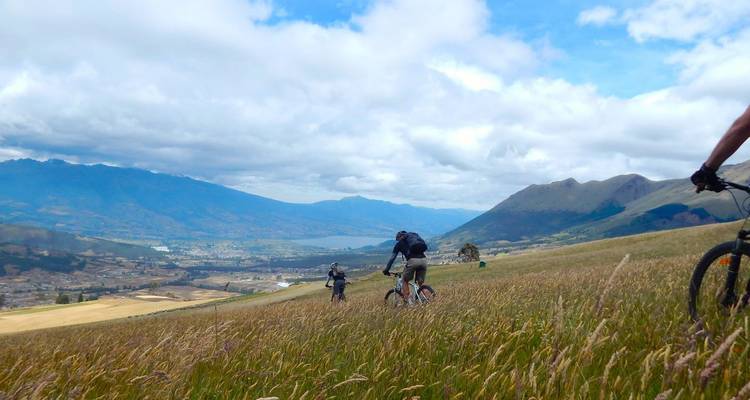 Groupe de cyclistes descendant une colline herbeuse avec des montagnes au loin.
