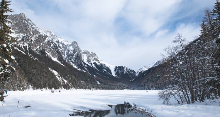 Menschen, die auf einem zugefrorenen See Schlittschuh laufen, umgeben von schneebedeckten Bergen.